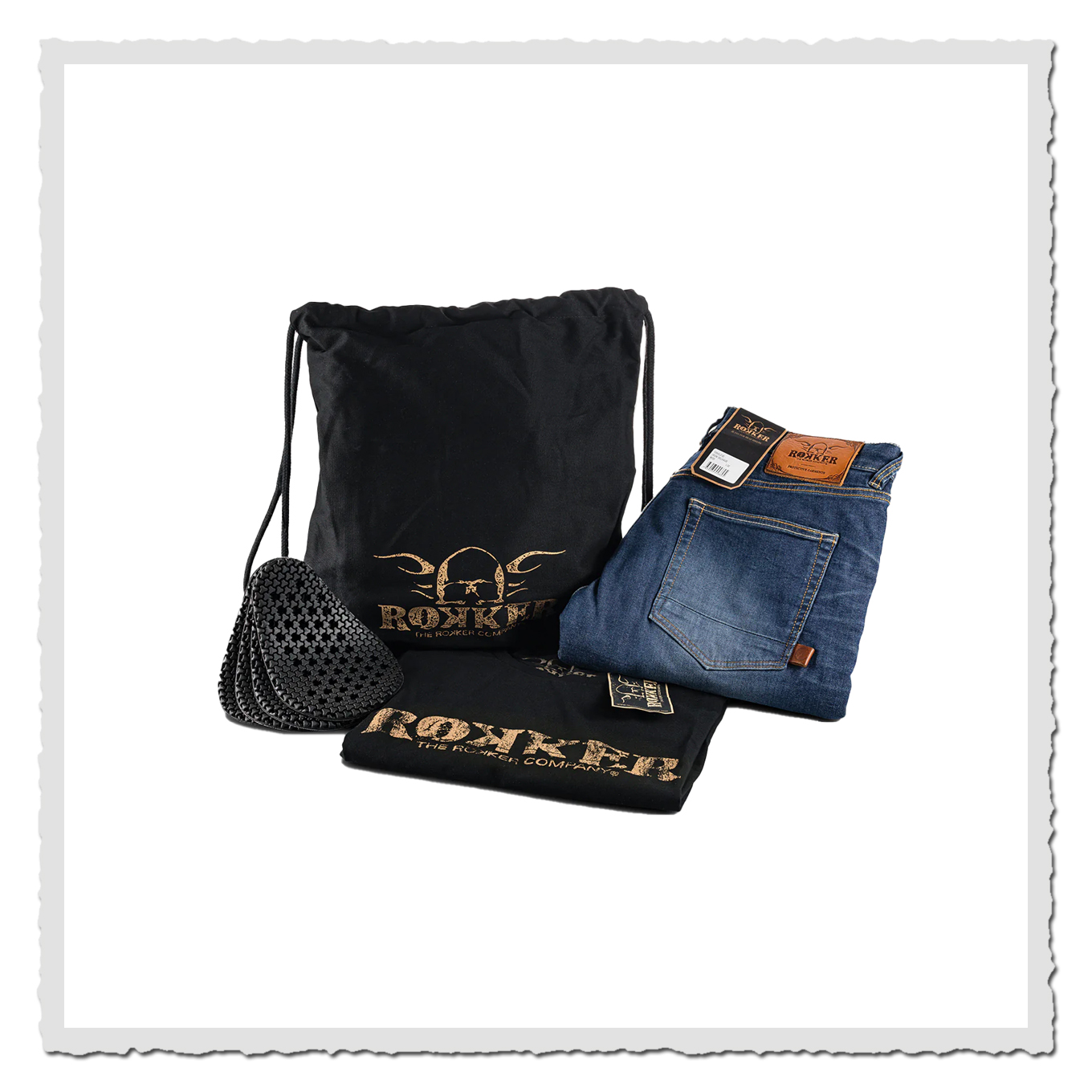 Setfoto: gefaltete Jeans neben schwarzem Rokker-Beutel, T-Shirt und Schutzpads auf Weiß.